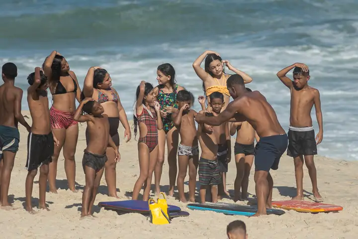 Crianças e instrutor em alongamento na Praia de São Conrado com pranchas de bodyboard