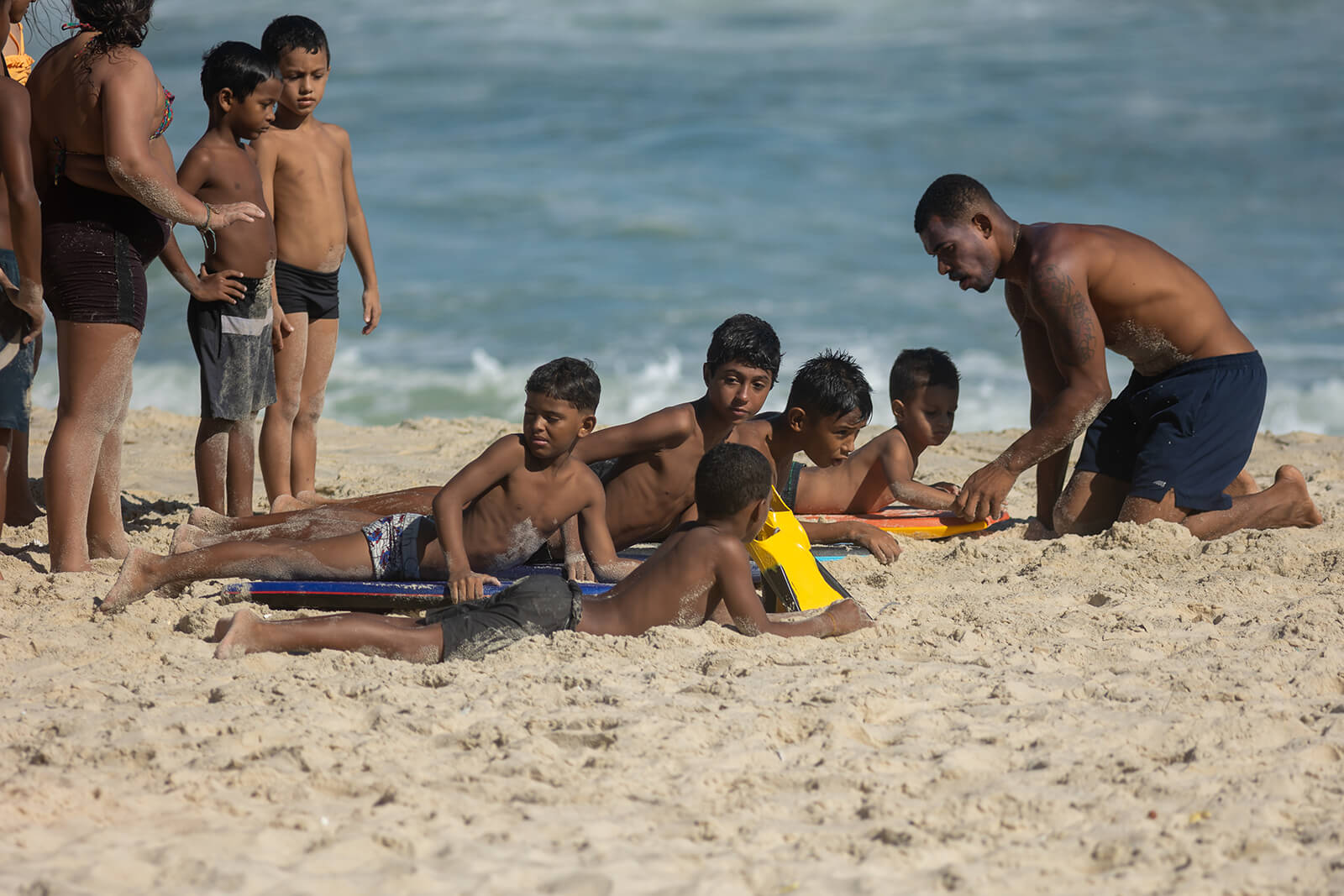 Instrutor orientando crianças deitadas em bodyboards na areia